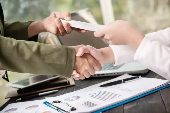 Únete al futuro de las finanzas sostenibles. Primer plano de un apretón de manos y el intercambio de un contrato entre profesionales con documentos financieros sobre una mesa.