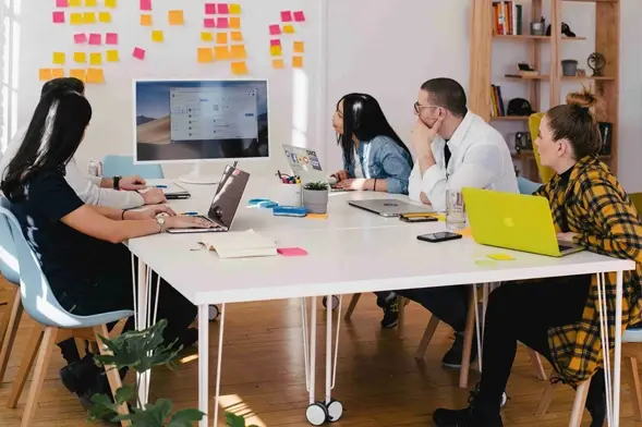 Diverse team collaborating around a table with laptops and sticky notes in a creative workspace.