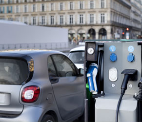 Estación de carga para vehículos eléctricos apoyando la movilidad sostenible en edificios. Estación de carga para vehículo eléctrico con coche compacto en entorno urbano.