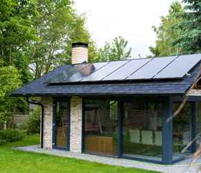 Casa con paneles solares que demuestra soluciones de eficiencia energética. Casa moderna con paneles solares en el techo rodeada de árboles